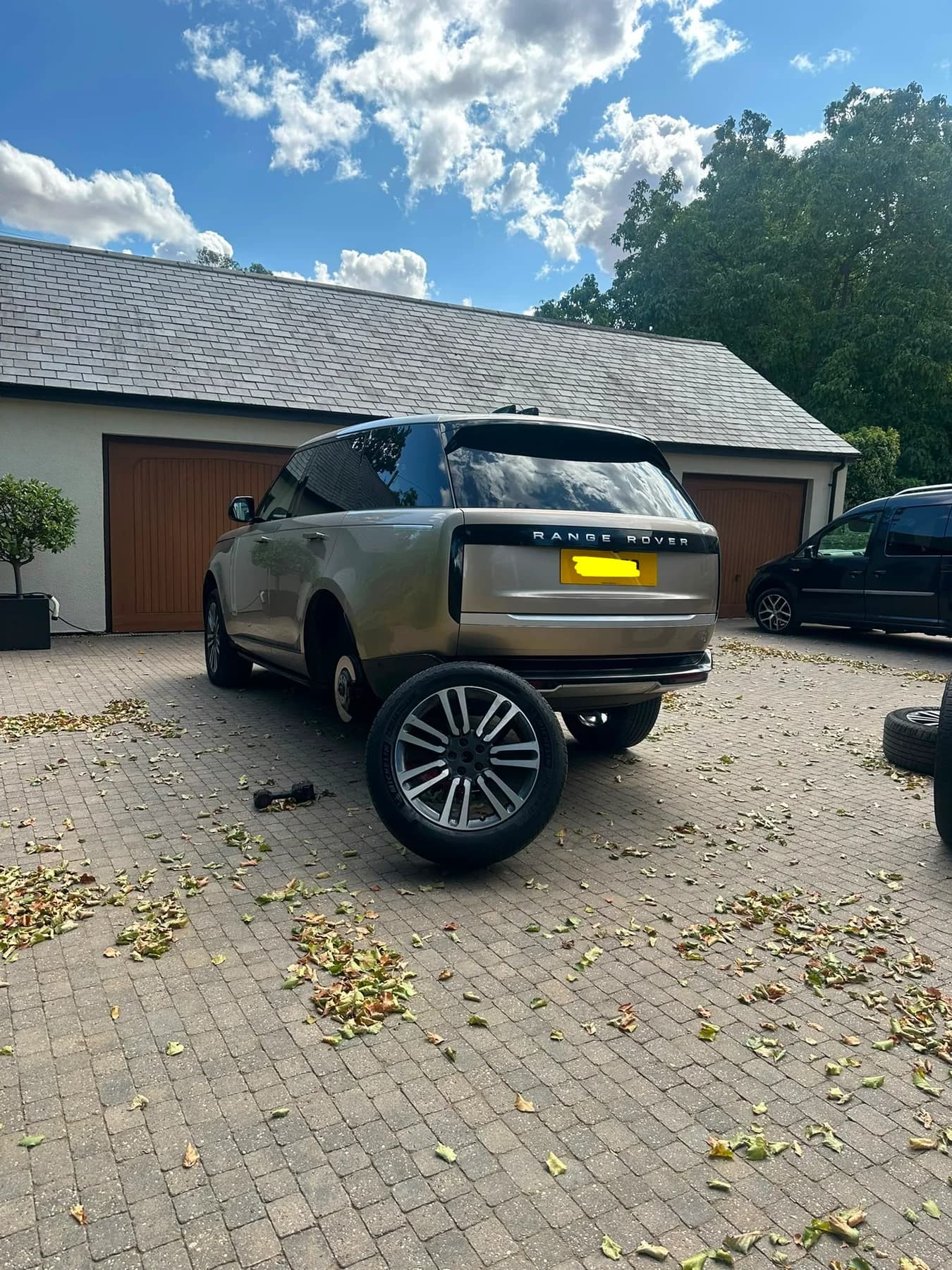 Range Rover on a paved driveway with a rear wheel removed for tyre work