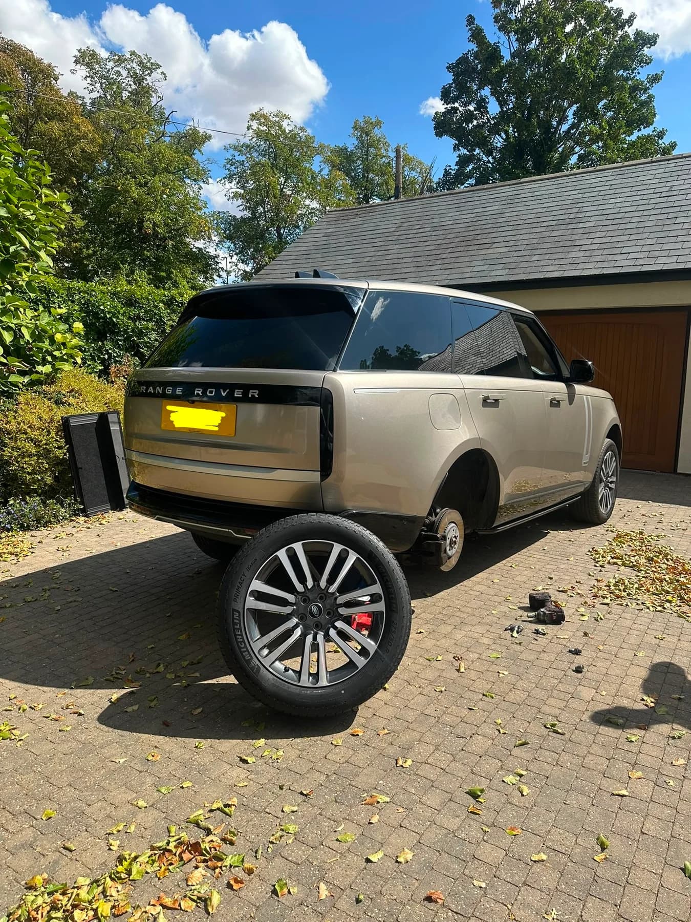 Gold Range Rover on a driveway with a rear wheel off beside the car