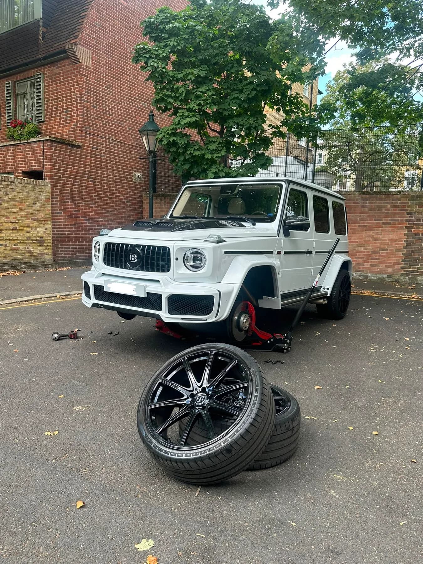 White off-road vehicle raised for a wheel change, with the removed wheels and tools alongside