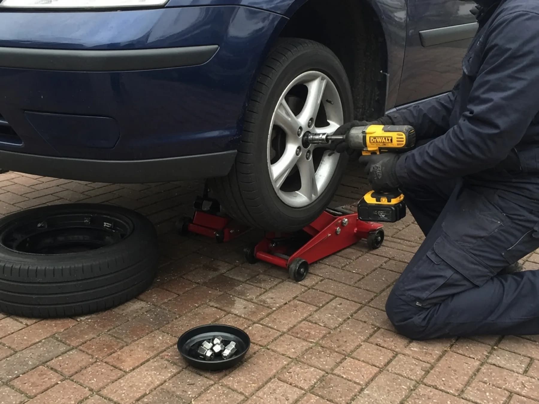 Service illustration: a fitter tightening wheel nuts on a complete tyre and alloy at a car